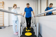 © wedmoments.stock - Male patient performing balance exercises on a stability platform with assistance from a female therapist in a rehabilitation center with mirrors and exercise equipment visible