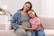 © New Africa - Pregnant woman and her daughter sitting on sofa at home