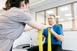 © wedmoments.stock - Male patient in blue shirt performs upper body rehabilitation exercises with resistance bands while seated in a bright physical therapy clinic with modern equipment