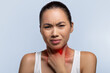 © Prostock-studio - A woman stands with a pained expression while holding her neck. She appears to be experiencing throat discomfort.
