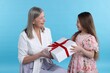© New Africa - Little girl greeting her grandmother with gift on light blue background