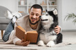 © Pixel-Shot - Handsome young man lying on floor and reading book with cute husky dog at home
