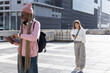 © wavebreak3 - Two female students on tiled plaza left checking watch with files right scrolling phone, copy space