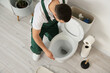 © Pixel-Shot - Male plumber repairing toilet in restroom, top view