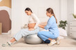 © Pixel-Shot - Young doula with pregnant woman training on fitball in bedroom