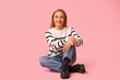 © Pixel-Shot - Beautiful mature woman in stylish striped sweater sitting on pink background