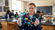 © Yuliani - Young female student in a lab coat and safety glasses holding a molecular model in a science classroom