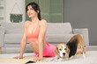 © Pixel-Shot - Young sporty woman with adorable Beagle dog stretching on yoga mat in living room