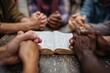 © Ibnu - Diverse hands clasped around an open book, gathered for prayer or religious study