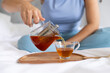 © Wavebreak Media - Glass teapot is pouring amber tea gently into clear glass cup on wooden tray on bed