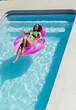 © Wavebreak Media - African American woman reclining on pink float wearing green bikini, holding glass at private pool
