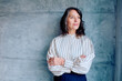 © we.bond.creations - Mature woman with gray hair crossing arms, looking away thoughtfully against a concrete wall, embodying professional confidence and contemplation