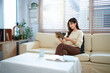 © Stella 16 - A woman smiles while sitting and relaxing on a couch in a living room, holding a tablet device