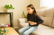 © AntonioDiaz - Little girl feeling stomach ache on sofa at home, experiencing abdominal pain and health problem
