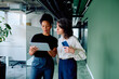 © we.bond.creations - Two diverse businesswomen collaborating and sharing ideas with a digital tablet while walking in a modern corporate office corridor