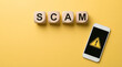 © Gambar - Scam Alert: Smartphone with Warning Sign and 'Scam' Wooden Blocks