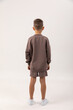 © Irina Mikhailichenko - Rear view little boy wearing brown sweatshirt and shorts stands confidently on a light background, showcasing casual children's fashion and comfortable attire. High quality photo