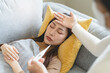 © Pormezz - Sick day at home in winter season. Young asian woman lying on the bed have a fever and her husband checking thermometer and measure body temperature.