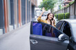 © Tj - Asian woman stepping out of a grey car on a city street, waving goodbye and communicating on her mobile phone, representing urban transportation services and connection
