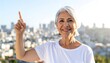 © birth7 - Senior woman smiling and pointing upward with city view symbolizing idea and optimism