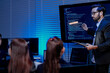 © ultramansk - A visionary male AI programmer in a futuristic setting with a headset actively presents complex code and data on a large screen discussing advanced machine learning algorithms.