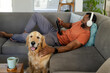 © Wavebreak Media - African American man lying on sofa at home, orange tee, holding tablet, petting dog, copy space