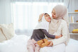 © DG PhotoStock - Asian Muslim daughter giving gift surprise to mother indoor family moment