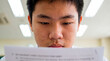 © Xenia - Stressed Asian student sweating while reading difficult exam paper. Anxiety and pressure concept