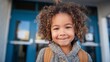© VictorCanalesStudio - Young girl with curly hair and a backpack smiling in front of a blue school door