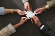 © New Africa - Team building. Group of businesspeople holding puzzle pieces together at dark textured table, top view
