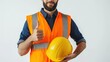 © Zabi - A man in a dark blue shirt and orange safety vest, holding a yellow hard hat, gives a positive thumbs-up gesture.