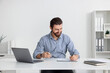© New Africa - Businessman working with laptop at table near white wall indoors