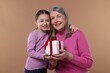 © New Africa - Little girl greeting her grandmother with gift on dark beige background