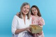 © New Africa - Little girl greeting her grandmother with gift on light blue background