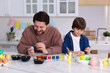 © New Africa - Easter celebration. Father and his son painting eggs at white marble table in kitchen