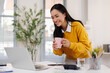© David - Cheerful young woman uses a laptop at desk in the office with cup of morning coffee.Financial and Accounting concept.
