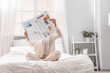 © Pixel-Shot - Young woman with newspaper sitting in bedroom