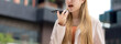 © NT_studio - Young caucasian businesswoman using voice message on smartphone with chatbot or AI outdoors in city, business woman speaking on smart phone with voice assistant AI in urban, artificial intelligence.