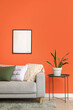 © Pixel-Shot - Comfortable grey sofa with soft pillows and table near orange wall in living room