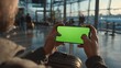 © InfiniteStudio - Passenger plays a game on smartphone in modern airport terminal near boarding gate with bright green screen