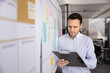 © fizkes - Business project analysis. Serious mid adult man market analyst operations manager review data on paper clipboard compare update information with workflow structure on agile planning board. Copy space