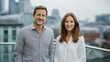© id512 - Confident young business man and woman standing on city rooftop, professional colleagues smiling at camera in urban office district. Male and female entrepreneurs in smart casual attire posing outdoor