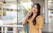 © Art_Photo - Beautiful young asian woman wearing yellow plaid dress standing near glass railing in shopping mall, Happy female fashion model smiling with hand on face, Lifestyle, summer fashion and beauty concept
