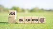 © Jamela - Wooden blocks with goal plan action words and target symbol on grass with 2026 new year stack in bright outdoor setting