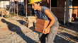© OlgaNeuroArt - Female construction worker carrying a stack of bricks at a building site. Woman in hard hat performing manual labor. Industrial occupation concept