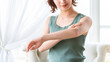 © Trickster* - 自然光の室内で、腕の肌をケアして確認する若い女性, Young woman checking and caring for her arm skin indoors in natural light
