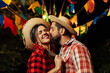 © kleberpicui - Brazilian couple wearing traditional rural costumes celebrating Festa Junina outdoors at night with colorful decorations and festive lights, representing affection and Brazilian cultural traditions.