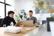 © Studio Marmellata - Two men collaborate on laptops at a wooden table in a bright, modern office space with plants and artwork.