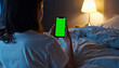 © ARVD73 - Mockup, green blank screen. Closeup of back view young white woman looking at her mobile phone and scrolling while lying in bed.