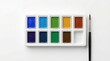 © Guzel - Top view of a watercolor paint set with ten vibrant colors and a brush on white, artistic design concept, creative tools, school supplies.